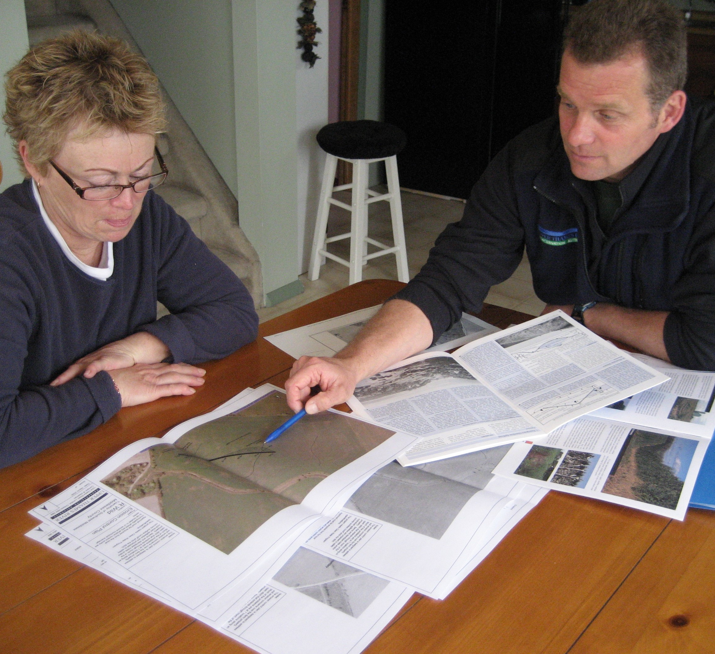 UTRCA staff and a landowner sit at a table and look at air photos and information about a farm
